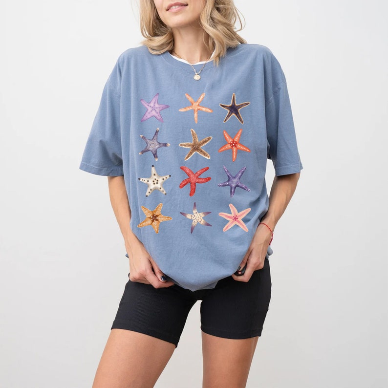 May include: A light blue t-shirt with a pattern of colorful starfish. The shirt has a relaxed fit and short sleeves.