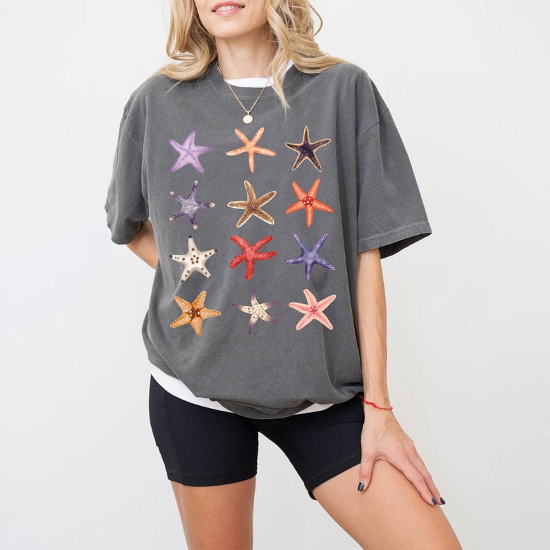 May include: A charcoal grey t-shirt with a pattern of colorful starfish. The shirt has a relaxed fit and short sleeves.