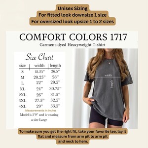 Puede incluir: Camiseta gris Comfort Colors 1717 de tejido grueso. La imagen incluye una tabla de tallas con medidas en pulgadas, desde la talla S hasta la 4XL. La modelo mide 1,75 m y lleva una talla L. El texto aconseja medir una camiseta favorita para un ajuste perfecto.