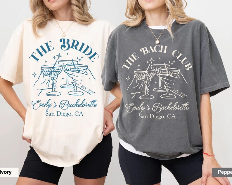 May include: Two t-shirts with a bachelorette party theme. The white t-shirt says "The Bride" with a design of four martini glasses and the text "Emily's Bachelorette, San Diego, CA". The gray t-shirt says "The Bach Club" with a design of four martini glasses and the text "Emily's Bachelorette, San Diego, CA".