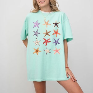 May include: A light blue t-shirt with a pattern of 12 colorful starfish. The starfish are arranged in a grid pattern on the front of the shirt.