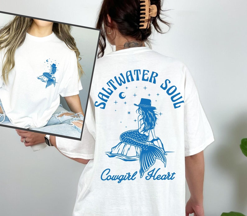 Peut inclure: T-shirt blanc avec un graphique bleu d'une sir&egrave;ne portant un chapeau de cow-boy et le texte "Saltwater Soul Cowgirl Heart".