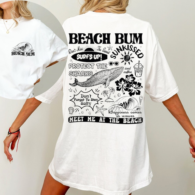 May include: White oversized t-shirt featuring a black graphic on the back with the words "Beach Bum" and beach-themed illustrations. The front of the shirt has a small graphic of a wave and the words "Beach Bum".