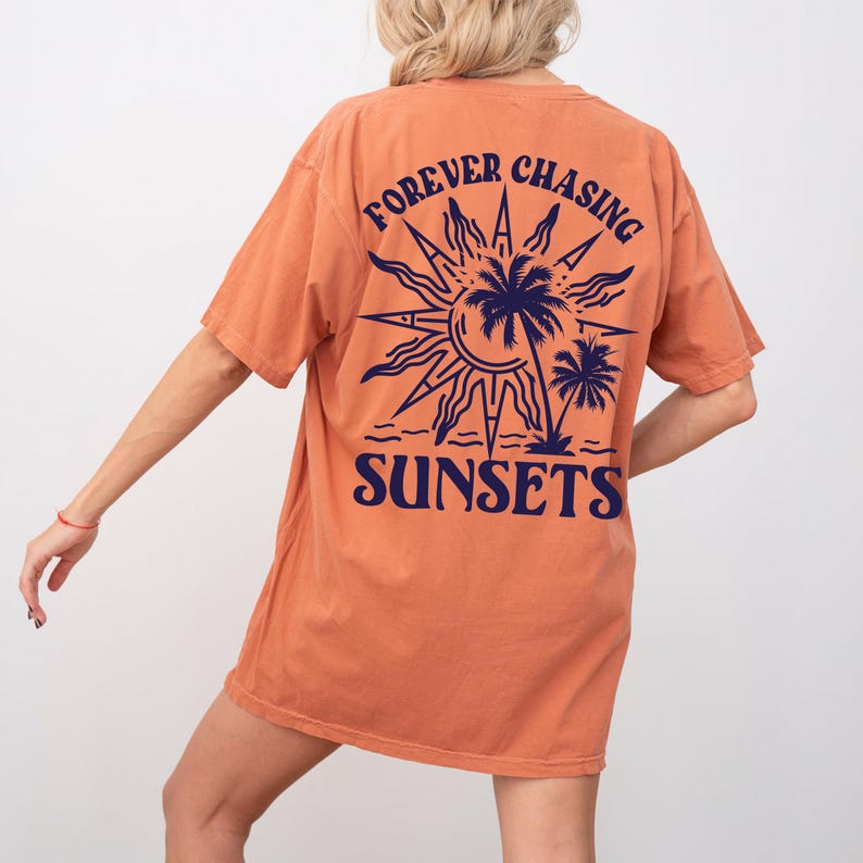 Puede incluir: Camiseta naranja con un gr&aacute;fico de un sol, palmeras y el texto "FOREVER CHASING SUNSETS" impreso en la espalda.
