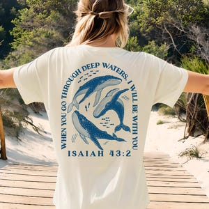May include: White t-shirt with a blue graphic of whales swimming in a circle with the text "WHEN YOU GO THROUGH DEEP WATERS. I WILL BE WITH YOU ISAIAH 43:2"