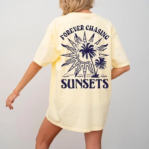 Puede incluir: Una camiseta amarilla con un gr&aacute;fico azul marino de un sol, palmeras y el texto "FOREVER CHASING SUNSETS".