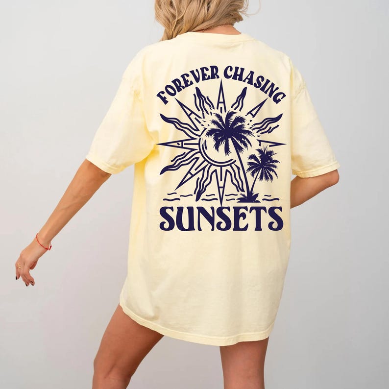 Puede incluir: Una camiseta amarilla con un gr&aacute;fico azul marino de un sol, palmeras y el texto "FOREVER CHASING SUNSETS".