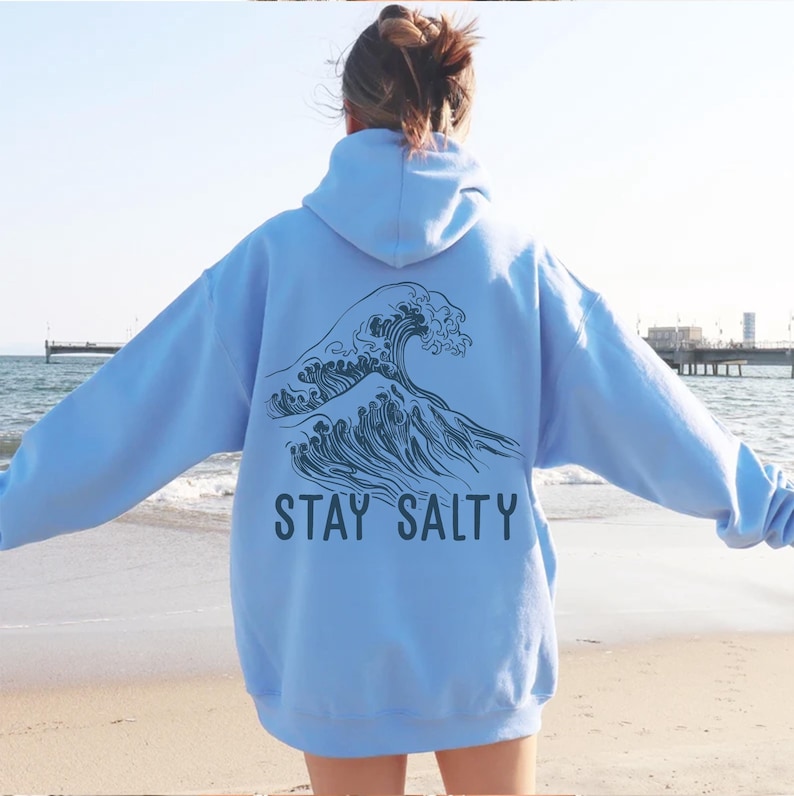 May include: A light blue hoodie with a graphic of a large wave and the text "STAY SALTY" printed on the back.