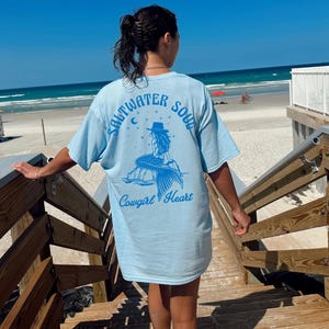 Peut inclure: T-shirt bleu clair avec un graphique de sir&egrave;ne et le texte "Saltwater Soul Cowgirl Heart".