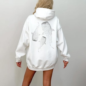 May include: White hoodie sweatshirt featuring a black and white illustration of three whale sharks on the back. The whale sharks are depicted with dotted patterns. The hoodie has a hood and long sleeves.