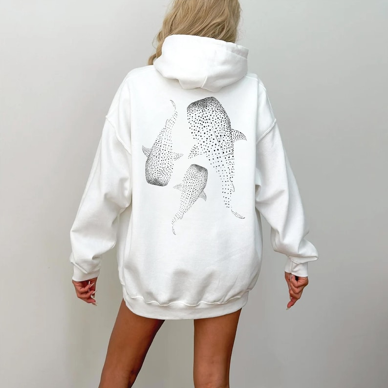 May include: White hoodie sweatshirt featuring a black and white illustration of three whale sharks on the back. The whale sharks are depicted with dotted patterns. The hoodie has a hood and long sleeves.