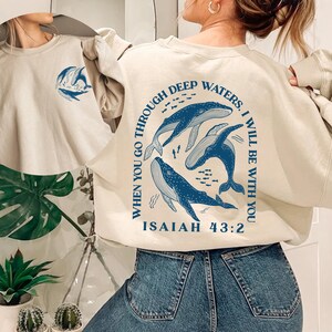May include: A beige sweatshirt with a blue whale graphic and the text "When you go through deep waters, I will be with you. Isaiah 43:2"
