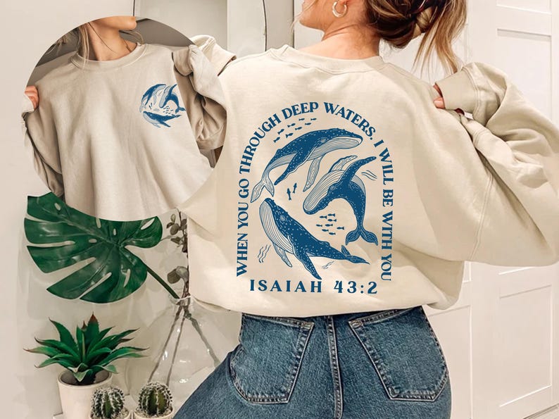 May include: A beige sweatshirt with a blue whale graphic and the text "When you go through deep waters, I will be with you. Isaiah 43:2"
