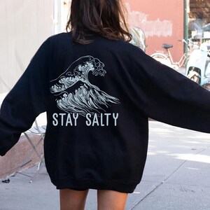 May include: Black long-sleeve sweatshirt with a white graphic of a wave and the text "STAY SALTY".
