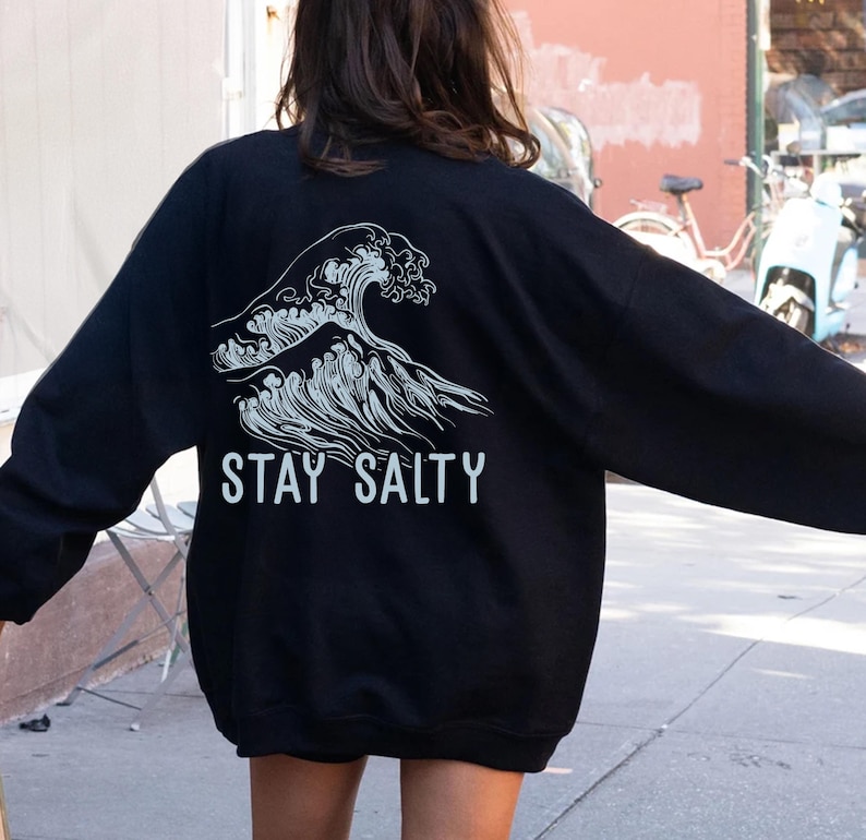 May include: Black long-sleeve sweatshirt with a white graphic of a wave and the text "STAY SALTY".