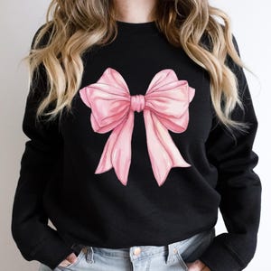 May include: A black sweatshirt with a large pink bow printed on the front.
