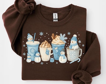 May include: A dark brown sweatshirt featuring a winter-themed graphic. The design includes various cups of hot beverages, snowmen, and snowflakes in shades of blue, white, and brown. The sweatshirt has long sleeves and a crew neck.