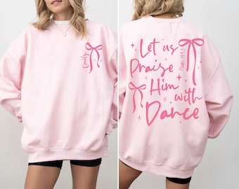 May include: A light pink sweatshirt with a bow and the name "Emily" printed on the front. The back of the sweatshirt features the text "Let us Praise Him with Dance" and "Psalm 149:3" in pink.