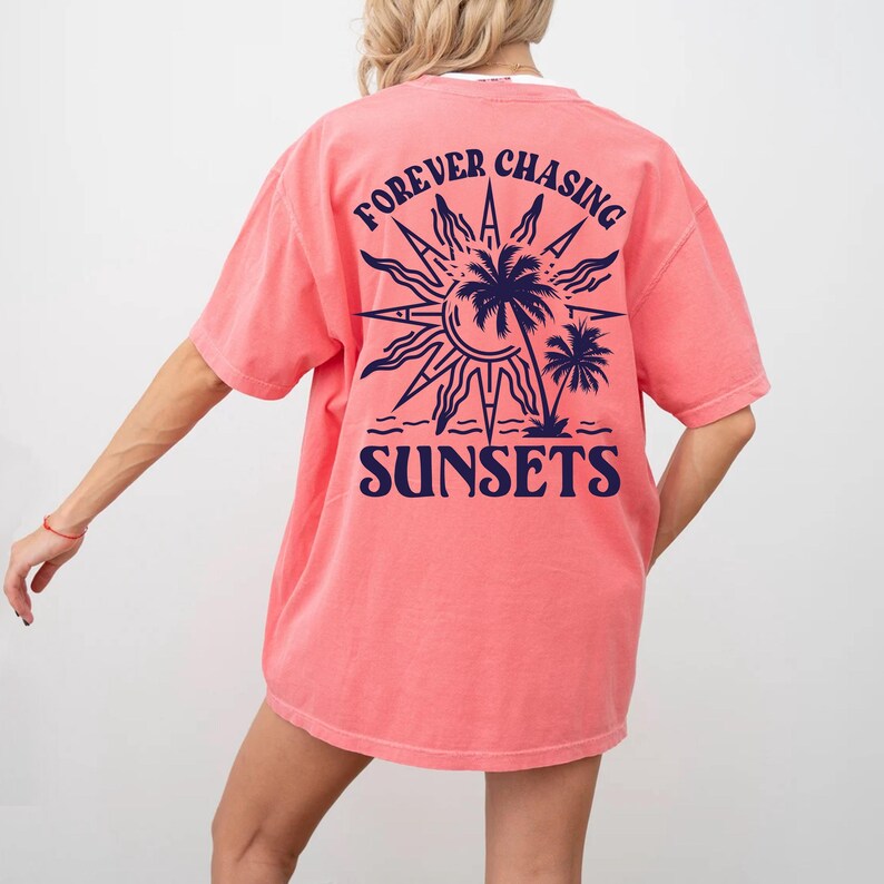 Puede incluir: Una camiseta de color rosa coral con un gr&aacute;fico azul marino en la espalda. El gr&aacute;fico presenta un sol con palmeras y el texto "FOREVER CHASING SUNSETS".