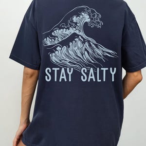 May include: A navy blue t-shirt with a graphic of a wave and the text "STAY SALTY" printed on the back.