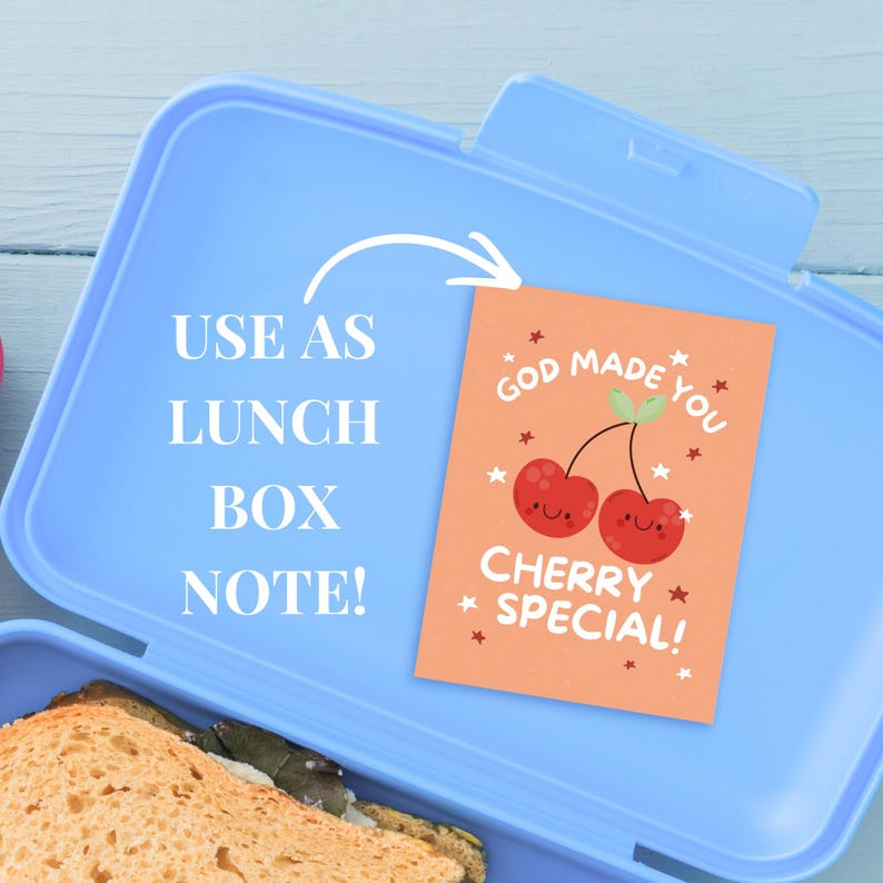 Peut inclure: Une bo&icirc;te &agrave; lunch bleu clair avec un sandwich &agrave; l'int&eacute;rieur. Une petite carte orange avec le texte "GOD MADE YOU CHERRY SPECIAL!" et deux cerises souriantes est &agrave; l'int&eacute;rieur. Le texte "USE AS LUNCH BOX NOTE!" est &eacute;galement visible.