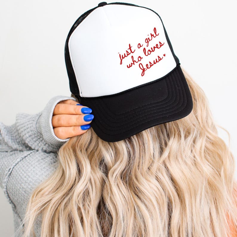 Op de afbeelding: Een zwart-witte truckercap met een wit voorpaneel en een zwart mesh achterpaneel. Het voorpaneel heeft een rode geborduurde tekst die "just a girl who loves Jesus." luidt.