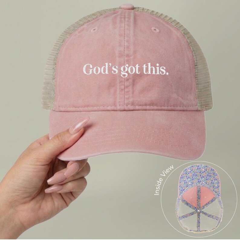 May include: A pink trucker cap with the text "God's got this." The cap features a mesh back and a curved peak. The inside of the cap has a floral pattern.