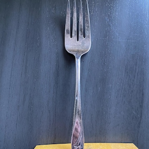May include: A silver fork with a floral design on the handle. The fork is sitting on a yellow box.