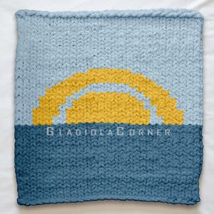 May include: A knitted square blanket with a sunrise design. The top half is light blue, the bottom half is dark blue, and a yellow sun is in the middle. The text "GLADIOLACORNER" is at the bottom.