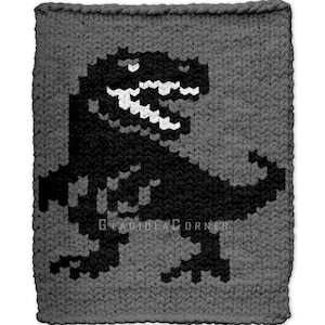 Può includere: Una coperta grigia lavorata a maglia con un design pixelato di Tyrannosaurus Rex nero. Il dinosauro ha denti bianchi ed è ambientato su uno sfondo grigio uniforme. Il testo "GLADIOLACORNER" è visibile in basso.