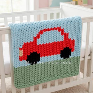 May include: A handmade, chunky knit baby blanket featuring a red car design on a blue sky background and green grass. The blanket is displayed over the side of a white crib. The text "GLADIOLA CORNER" is visible.