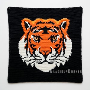 Op de afbeelding: Een vierkante, zwarte gehaakte kussenhoes met een tijgergezicht. De tijger is oranje, wit en zwart, met gedetailleerde ogen en strepen. Het haakwerk is strak en gelijkmatig, waardoor een duidelijk beeld ontstaat.