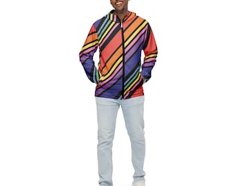 Può includere: Una persona indossa una giacca a vento con cappuccio e cerniera, con un vivace motivo a righe diagonali nei colori dell'arcobaleno. La giacca è abbinata a jeans azzurri e scarpe da ginnastica bianche.