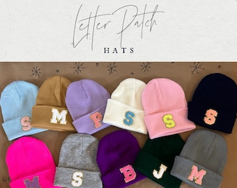 May include: Ten knit beanies with different colored felt letter patches. The letters are: S, M, P, S, S, S, M, J, B, and M. The beanies are in various colors including light blue, brown, purple, white, pink, grey, black, and neon pink.