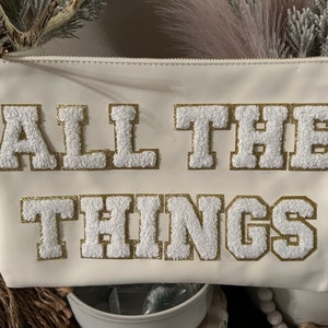 May include: White zippered pouch with the words "ALL THE THINGS" in gold and white fluffy letters.