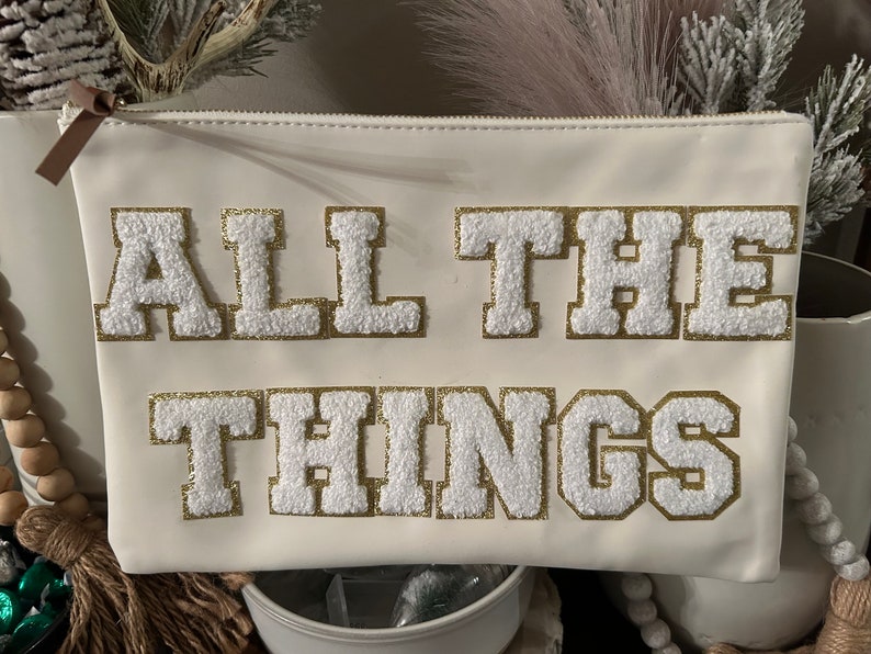 May include: White zippered pouch with the words "ALL THE THINGS" in gold and white fluffy letters.