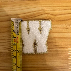 May include: White felt letter W with gold glitter trim, measured with a yellow tape measure. The letter is approximately 2 inches tall.