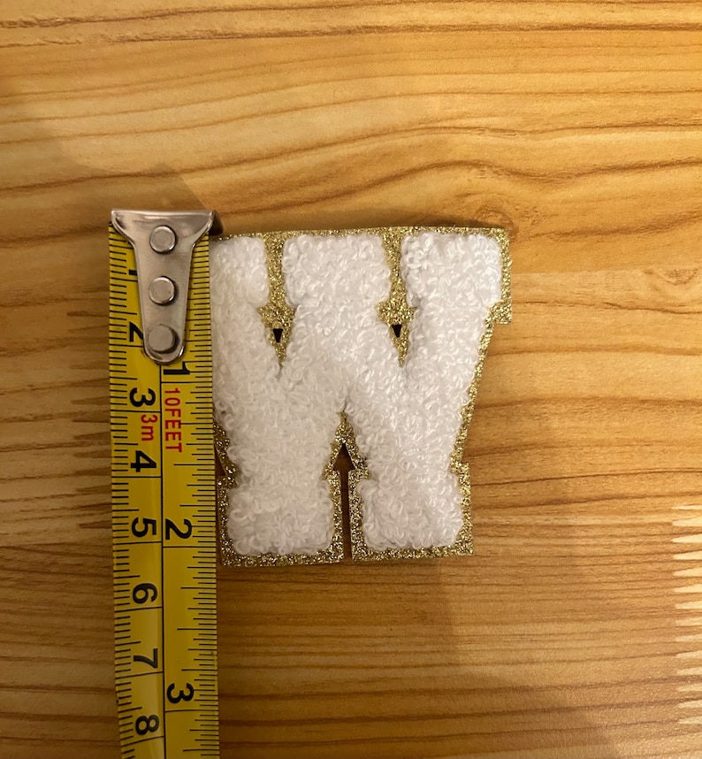 May include: White felt letter W with gold glitter trim, measured with a yellow tape measure. The letter is approximately 2 inches tall.