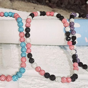 May include: Three beaded necklaces with different color combinations. The first necklace is turquoise and pink, the second is black and white, and the third is purple and white.