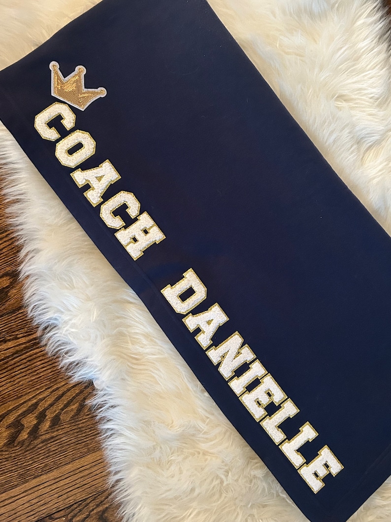 May include: Navy blue blanket with white text that reads "Coach Danielle" and a gold crown.
