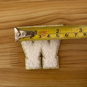 May include: White felt letter W with a gold glitter outline. The letter is approximately 2 inches tall.