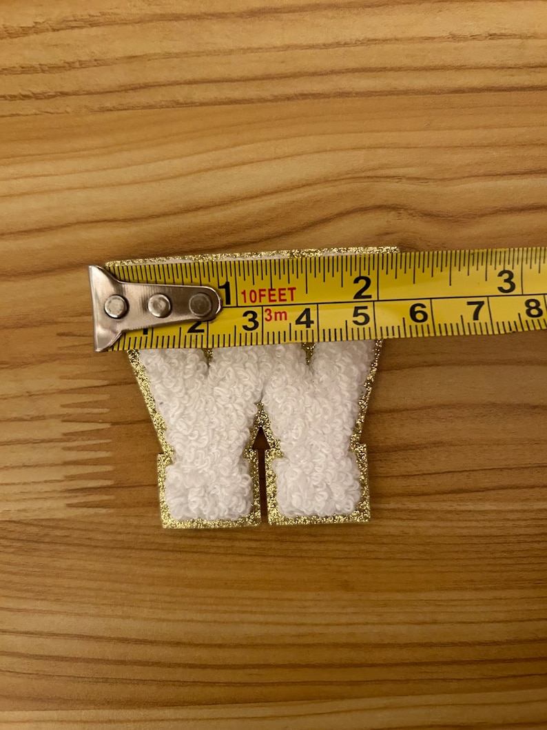 May include: White felt letter W with a gold glitter outline. The letter is approximately 2 inches tall.