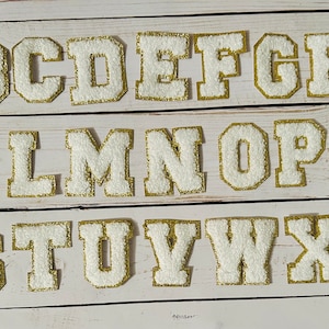 May include: White felt letters with gold outlines, from A to Z, arranged in three rows. The letters are uppercase and have a classic, collegiate style.