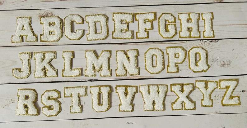May include: White felt letters with gold outlines, from A to Z, arranged in three rows. The letters are uppercase and have a classic, collegiate style.