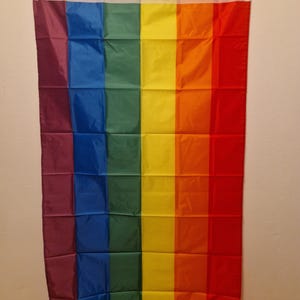 Puede incluir: Una bandera del orgullo arcoíris con seis franjas horizontales en los colores rojo, naranja, amarillo, verde, azul y morado.