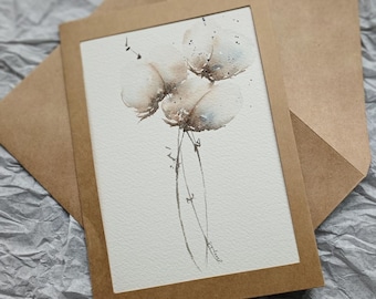Op de afbeelding: Een aquarel schilderij van pluizige, beige bloemen met bruine stelen en blauwe accenten. Het kunstwerk is geplaatst in een bruine lijst en op een witte achtergrond. Een bruine envelop bevindt zich achter het kunstwerk.