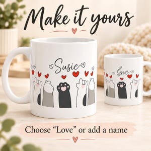 Op de afbeelding: Twee witte keramische mokken met een afbeelding van opgeheven kattenpootjes en rode hartjes. De grotere mok toont de naam Susie, terwijl de kleinere mok het woord love bevat. De tekst op de afbeelding luidt Make it yours en Choose Love or add a name.