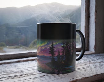 Pode incluir: Caneca de café preta com um design de paisagem com um céu colorido, árvores e água. A caneca está em uma janela de madeira com vista para a montanha ao fundo. Vapor sobe da caneca.