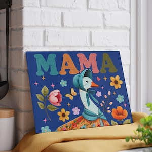 May include: A blue canvas print featuring a goose wearing a bonnet and floral dress. The word "MAMA" is displayed in colorful, retro-style letters above the goose. Floral and butterfly illustrations surround the goose.