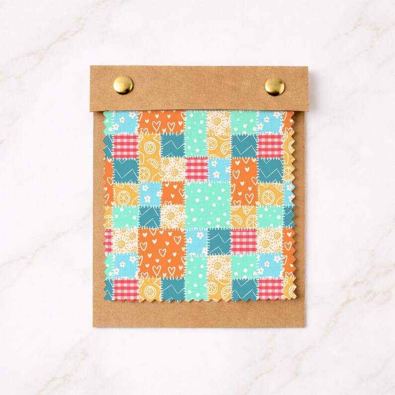 May include: A fabric swatch card featuring a patchwork design with various patterns. The patchwork includes squares of orange, blue, teal, and yellow fabrics. Some squares have heart, floral, and polka dot patterns. The card is held in a brown paper holder with gold fasteners.